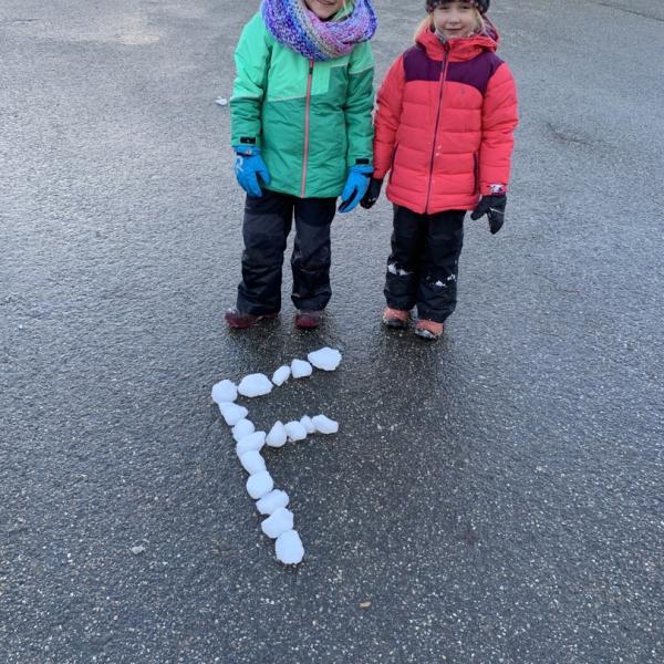 Zwei Mädchen haben auf dem Pausenhof den Buchstaben F aus Eisklötzen gelegt