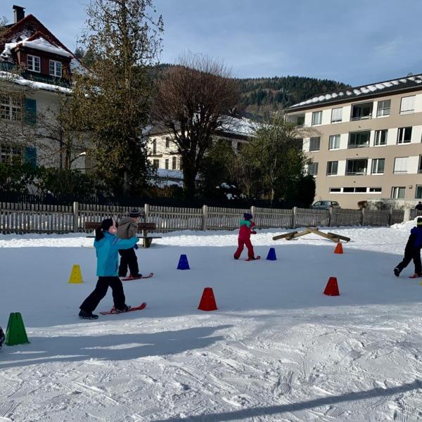 Kinder bewegen sich auf Mini-Skiern über den Pausenhof
