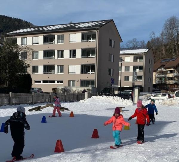 Kinder fahren auf Mini-Skiern über den Pausenhof